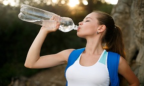 Pretty hiker girl drinking water. Thirsty woman tourist with backpack drinks water outdoors. Shapely female drinks clear water out of bottle backlit with sun. Refreshing healthy lifestyle concept